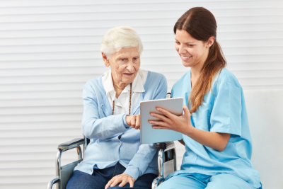 Curious senior citizen in wheelchair learns from caregiver dealing with tablet pc