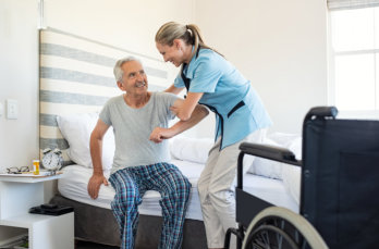 Smiling nurse assisting senior man getting up from bed.