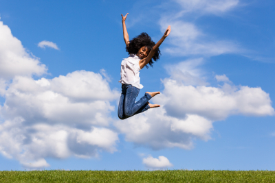  Outdoor portrait of a smiling teenage black girl jumping over a blue sky